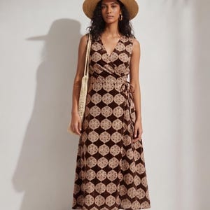 Puede incluir: Vestido cruzado sin mangas con estampado geométrico marrón y beige. El vestido se combina con un sombrero de paja, aros dorados, un bolso tejido y sandalias marrones. El vestido tiene un escote en V y un cierre de lazo en la cintura.