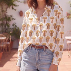 May include: A long-sleeved button-down shirt featuring a repeating yellow and brown floral block print pattern on a white background, paired with light blue denim shorts and a thin brown woven leather belt with a silver-toned metal buckle.