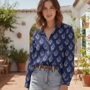 Può includere: Una camicia a maniche lunghe con bottoni in blu navy caratterizzata da un motivo floreale bianco ripetuto in stile cachemire, abbinata a pantaloncini di jeans lavaggio chiaro e una sottile cintura in pelle marrone con fibbia dorata.