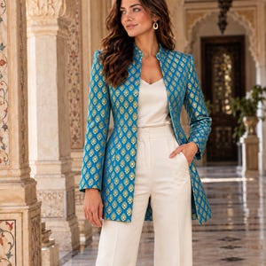 May include: A long-sleeved, open-front jacket in bright blue with a repeating gold teardrop pattern, paired with a cream-colored V-neck camisole and matching cream-colored wide-leg trousers. The jacket features a high collar and structured fit.