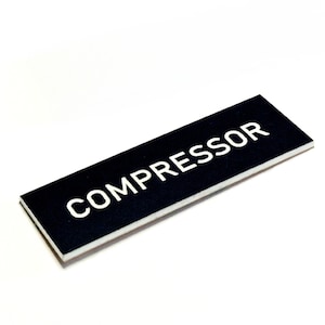 Peut inclure: Panneau rectangulaire noir avec le mot "COMPRESSEUR" en blanc. Le panneau a une bordure blanche et est posé sur un fond blanc. Le panneau est légèrement incliné.