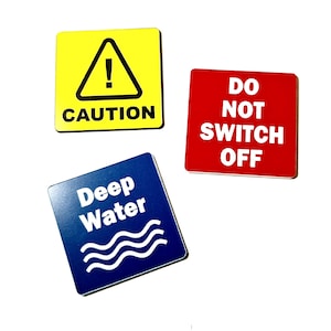 Peut inclure: Trois panneaux de signalisation carrés. Un panneau jaune avec un triangle noir et un point d'exclamation indique "ATTENTION". Un panneau rouge indique "NE PAS COUPER LE COURANT". Un panneau bleu avec des vagues blanches indique "Eau Profonde".