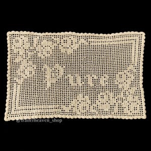 Peut inclure: Un napperon en crochet beige avec un bord festonné. Le napperon présente un motif floral délicat.