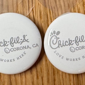 May include: Four white round buttons with the Chick-fil-A logo and the text "Love Works Here" and "Corona, CA".