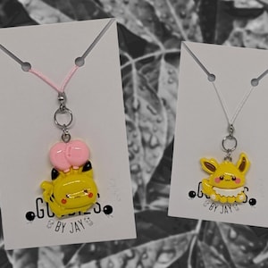 May include: Two necklaces with yellow cartoon character charms. One charm is a yellow character with pink ears and the other is a yellow character with white fur. Both necklaces have silver chains and are displayed on white cards with the text "Goodies by Jay".