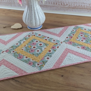 Peut inclure: Chemin de table matelassé avec un motif floral dans les tons de rose, jaune et bleu. Le chemin de table présente un motif géométrique avec des pièces maîtresses florales en forme de losange et des bordures blanches et roses. Environ 152 cm de long.