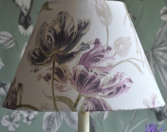May include: A white lampshade with a floral pattern featuring large purple and grey tulips. The lampshade has a conical shape and is made of fabric.