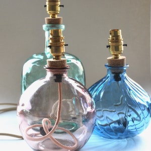 May include: Three decorative glass bottle lamps in shades of blue, green, and pink. Each lamp has a cork stopper, brass bulb holder, and a fabric-covered cord. The lamps are designed with a vintage aesthetic.