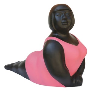 Op de afbeelding: Een zwart en roze keramisch beeld van een vrouw in een badpak. De vrouw zit met gekruiste benen en haar armen rusten op haar knieën.