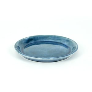 Op de afbeelding: Een ronde, ondiepe, blauwe keramische plaat met een glanzende afwerking. De plaat heeft een licht verhoogde rand en een glad, reflecterend oppervlak. De kleur varieert van licht- tot donkerblauw. Geschikt voor het serveren van voedsel.