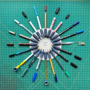 Könnte beinhalten: Eine Auswahl an bunten Stiften und Markern, die in einem Kreis um einen weißen Kreis mit dem Text "Adapter für Cricut" angeordnet sind.