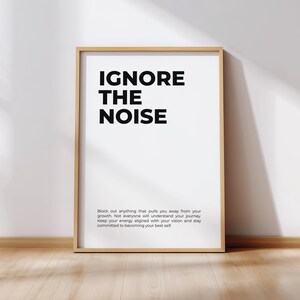 Könnte beinhalten: Ein gerahmter Druck mit den Worten "IGNORE THE NOISE" in fetten schwarzen Buchstaben auf weißem Hintergrund. Der Druck enthält auch eine motivierende Botschaft in kleinerer Schrift. Der Rahmen ist hellbraun, und der Druck lehnt an einer weißen Wand.