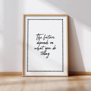 May include: A framed print with the quote "The future depends on what you do today" in black script. The white background is framed by a dotted border. The frame is a light wood color.