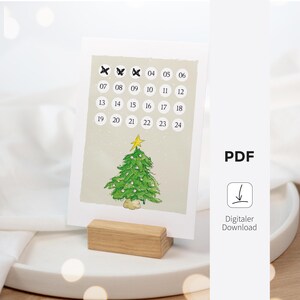 May include: A printable Christmas advent calendar with a hand-drawn illustration of a green Christmas tree with white ornaments and a gold star on top. The calendar features a grid of 24 circles with numbers 1 through 24. The text "PDF" and "Digitaler Download" is visible below the calendar.
