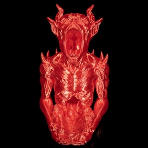 May include: A bright red, glossy figurine of a horned creature with a wide-open mouth, pointed ears, and spiked shoulders. The figure has a textured, muscular torso and holds a rounded, irregular object in its hands against a black background.