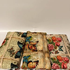 May include: Three rectangular pillows with butterfly and floral patterns. The pillows feature a vintage newspaper print background. The butterflies are in shades of blue, orange, and brown. Each pillow has a tag that reads "Hollie's Handmades."