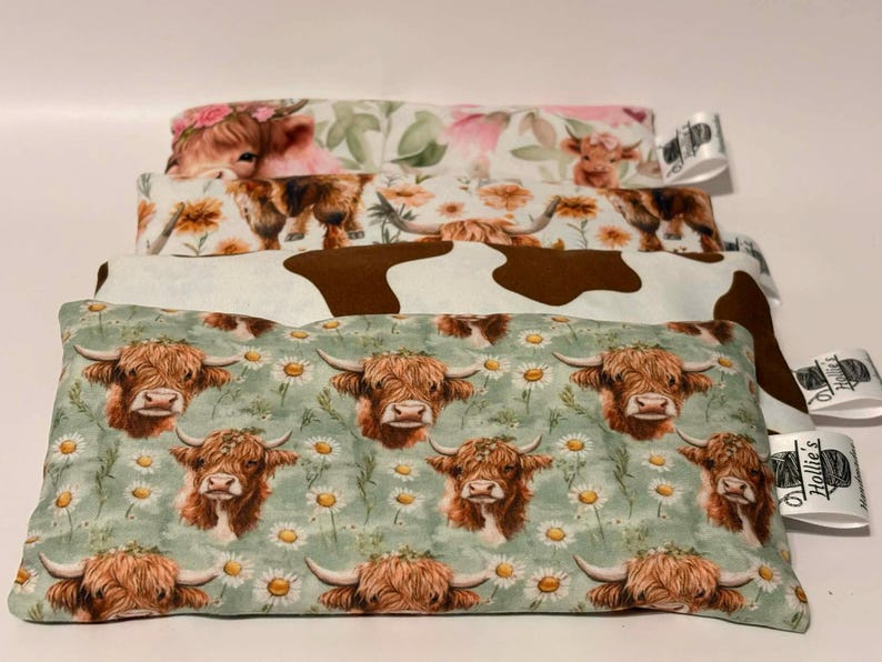 May include: A stack of four rectangular fabric items with various cow-themed patterns. The patterns include Highland cows, floral designs, and a cowhide print. The bottom item features Highland cows and daisies on a green background.