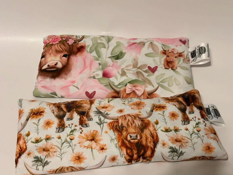 May include: Two rectangular pillows with Highland cow designs. One pillow features a cow with a floral crown and pink accents. The other pillow has a cow with orange flowers. Both pillows have a white background.
