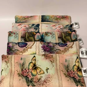 May include: A stack of rectangular, floral-patterned pillows. The pillows feature butterfly and flower designs in shades of yellow, pink, and blue on a cream background. Each pillow has a tag attached.