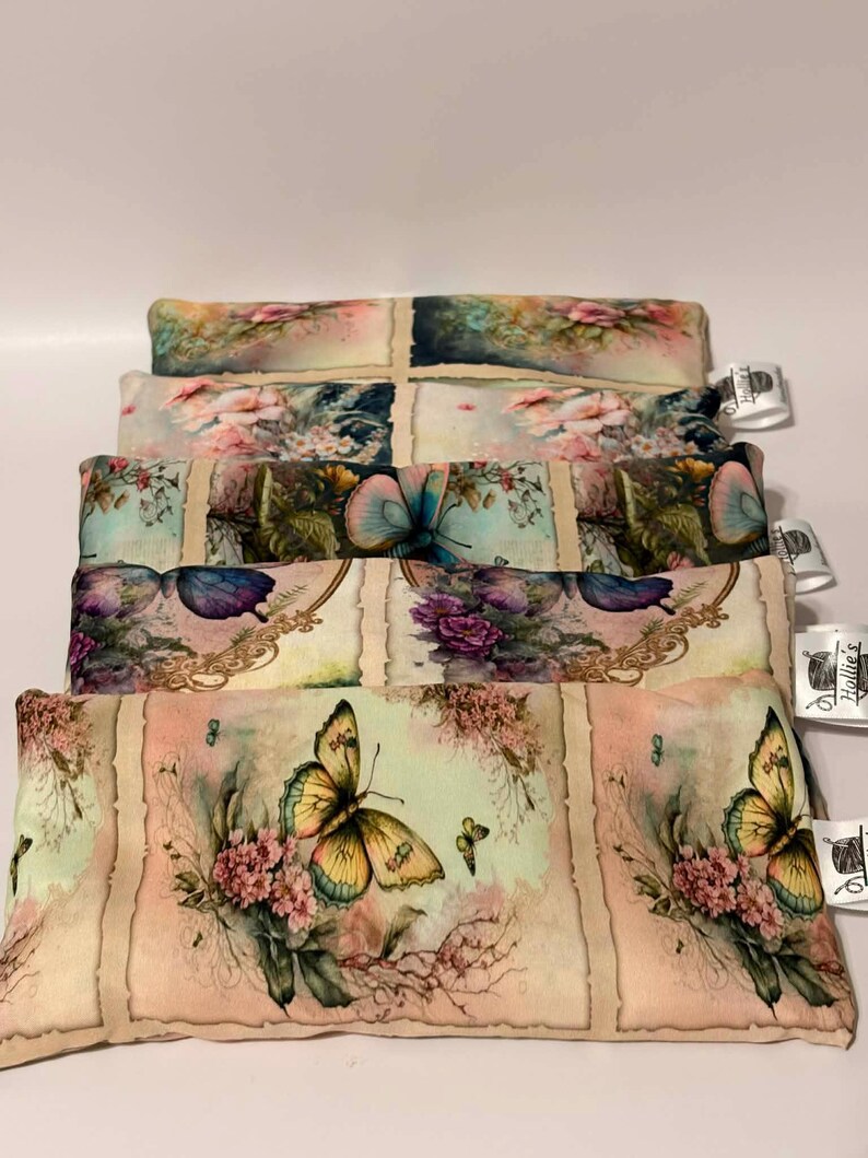 May include: A stack of rectangular, floral-patterned pillows. The pillows feature butterfly and flower designs in shades of yellow, pink, and blue on a cream background. Each pillow has a tag attached.