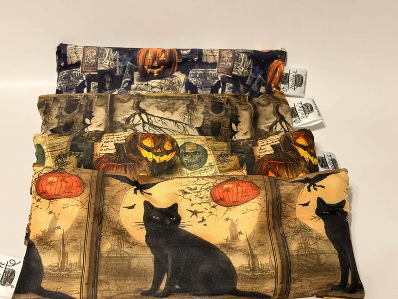 May include: Stacked Halloween-themed fabric pouches with various designs. The top pouch features a pumpkin and tombstone pattern. The middle pouch has a pumpkin, skull, and tree design. The bottom pouch showcases a black cat, bats, and a full moon.