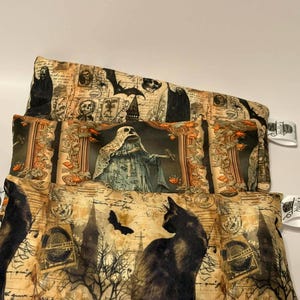 May include: Three Halloween-themed fabric pouches stacked on top of each other. The top pouch features a design with skulls and bats. The middle pouch has a ghost design. The bottom pouch has a black cat design.