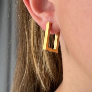 Puede incluir: Pendientes de aro cuadrados de oro. Los pendientes están hechos de metal grueso y sólido y tienen un diseño simple y moderno.