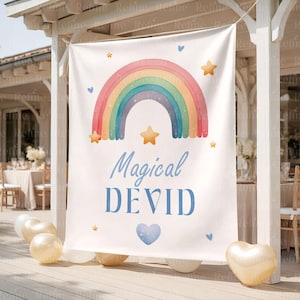Op de afbeelding: Een witte banner met een aquarel regenboog, sterren en harten. De banner leest "Magical DEVID" in blauw script. Gouden en witte ballonnen staan op de voorgrond, met een vage buitenomgeving op de achtergrond.