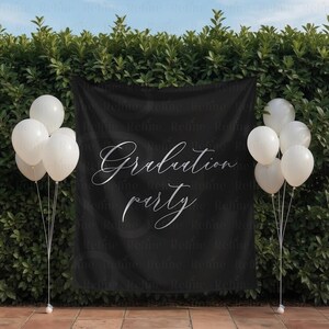 May include: A black banner with the words "Graduation party" in elegant silver script. White balloons are arranged on either side of the banner, creating a festive atmosphere. The backdrop is a lush green hedge.