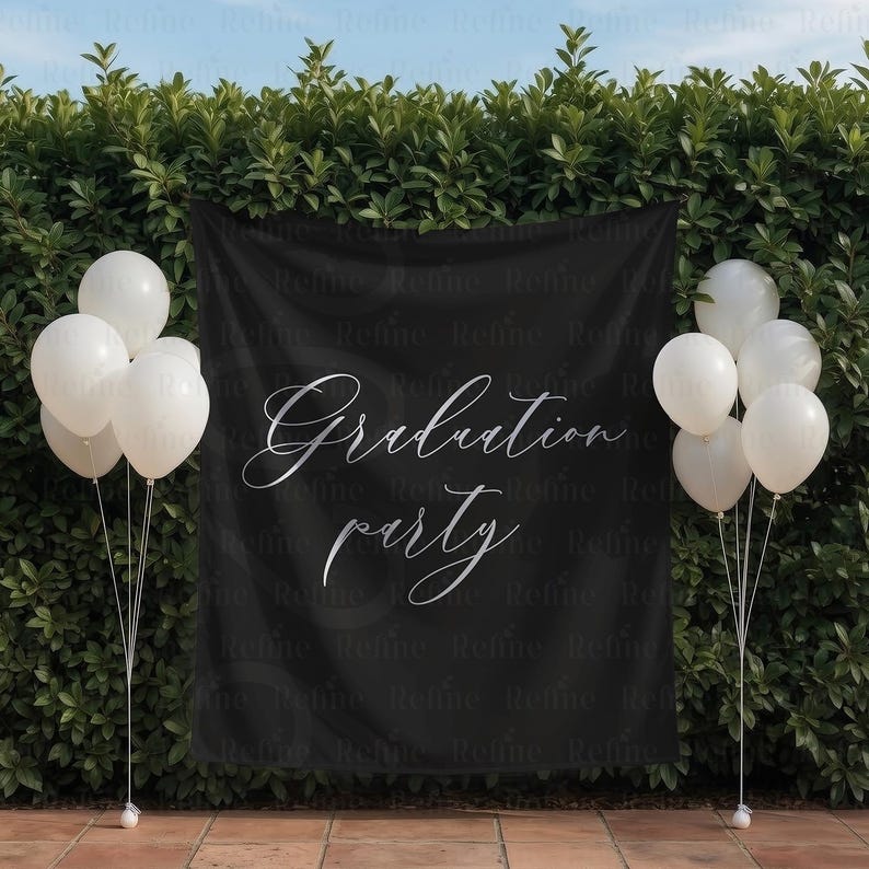 May include: A black banner with the words "Graduation party" in elegant silver script. White balloons are arranged on either side of the banner, creating a festive atmosphere. The backdrop is a lush green hedge.