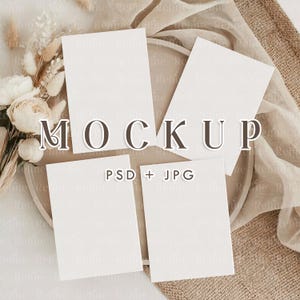 May include: A mockup scene featuring four blank white cards arranged on a neutral-toned plate, with the word "MOCKUP" overlaid. The cards are surrounded by dried flowers and fabric, with the text "PSD + JPG" visible.