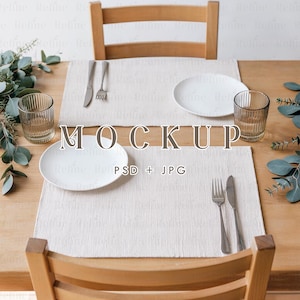 Może przedstawiać: Ustawienie stołu dla dwóch osób z białymi talerzami, teksturowanymi kremowymi podkładkami, szklankami i sztućcami. Na stole widnieją słowa "MOCKUP" i "PSD + JPG". Stół jest drewniany.