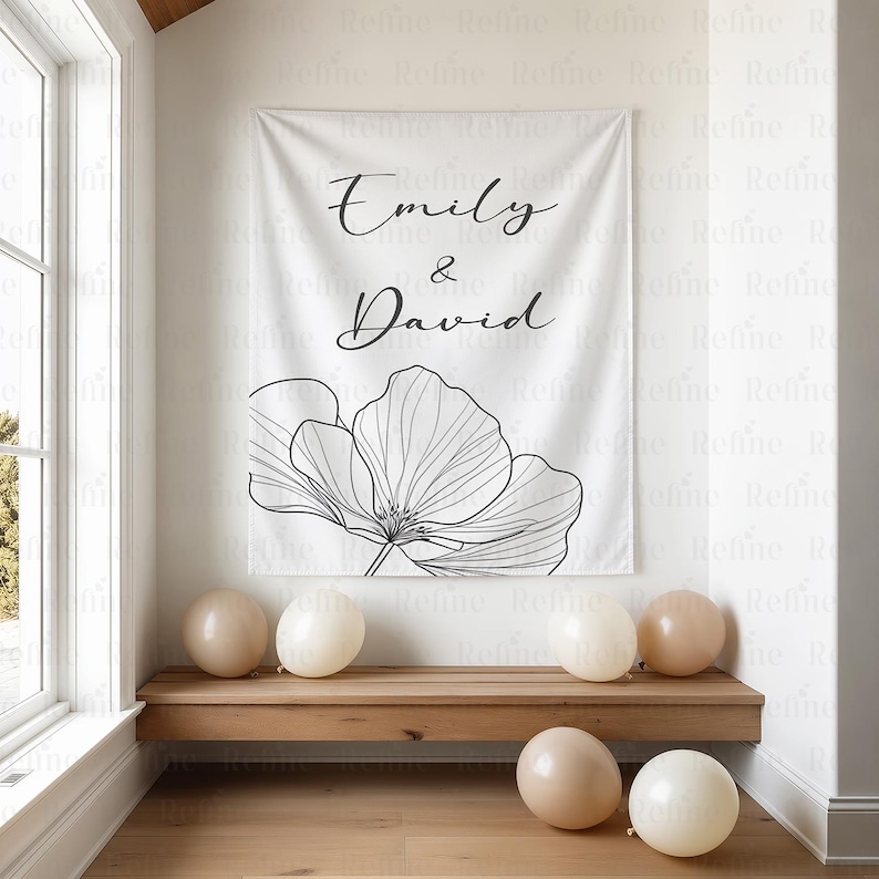 K&ouml;nnte beinhalten: Ein wei&szlig;es Banner mit den Namen "Emily & David" in eleganter Schrift und einem schwarz-wei&szlig;en Blumendesign. Mehrere beige Luftballons liegen auf dem Boden und eine Holzbank. Das Banner h&auml;ngt an einer wei&szlig;en Wand.