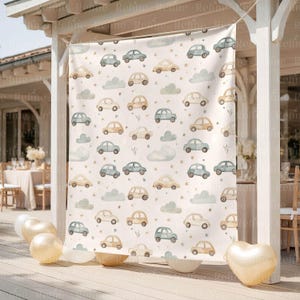 Op de afbeelding: Een cr&egrave;mekleurige stoffen achtergrond met een herhalend patroon van aquarel auto's in tinten blauw, beige en cr&egrave;me, samen met grijze wolken en kleine gouden sterren. De achtergrond hangt buiten, met ballonnen en een hartvormige ballon op de voorgrond.