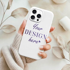 May include: A white phone case with a triple-lens camera design. The case features the text "Your DESIGN here" in purple script. The phone case is held in a person's hand.