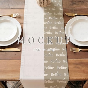 Könnte beinhalten: Ein Tisch-Setting-Mockup mit einem Holztisch, weißen Tellern, goldenem Besteck und einem Weidenkorb. Ein zweifarbiger Tischläufer mit dem Wort "Refine" wiederholt und dem Wort "MOCKUP" sichtbar.