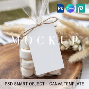 Puede incluir: Una bolsa transparente llena de malvaviscos, atada con hilo de bramante, y una etiqueta blanca en blanco. La palabra "MOCKUP" está impresa en la etiqueta. El texto "PSD SMART OBJECT + CANVA TEMPLATE" está en la parte inferior. El fondo incluye plantas secas.