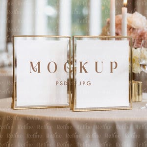 May include: Two gold-framed rectangular mockups with white inserts, displaying the word "MOCKUP" in brown. The frames are on a beige tablecloth, with blurred background elements including candles and flowers. The text "PSD" and "JPG" are also visible.
