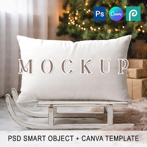 Puede incluir: Una almohada rectangular blanca con la palabra "MOCKUP" en letras marrones. La almohada descansa sobre un pequeño trineo de madera blanca desgastada. La imagen incluye el texto "PSD SMART OBJECT + CANVA TEMPLATE".