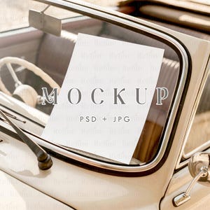 May include: A white rectangular card with the word "MOCKUP" in gray letters is placed inside the windshield of a vintage car. The card also has the text "PSD + JPG" in smaller gray letters.