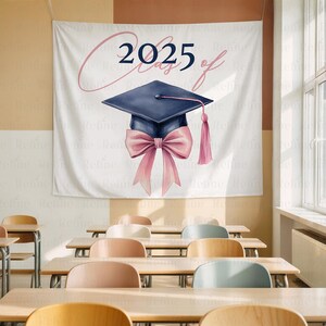 May include: A white banner with the text "2025 Class of" and a navy blue graduation cap with a pink bow and tassel. The banner is hanging in a classroom with wooden desks and chairs.