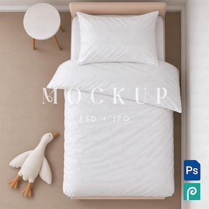 May include: A white bedding set featuring a pillow and a duvet cover on a bed frame, accompanied by a small white round side table and a plush white goose toy. The image includes the text MOCKUP PSD + JPG overlaid on the bedding.