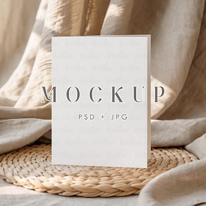 May include: A white card with the word "MOCKUP" in gray letters, with "PSD + JPG" below it. The card is on a woven mat, with a beige fabric in the background. The image is well-lit and suitable for product mockups.