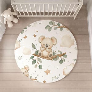 May include: A white round play mat with a koala bear design. The koala is brown and sitting on a branch with green leaves. The mat has a white background with brown clouds and stars.