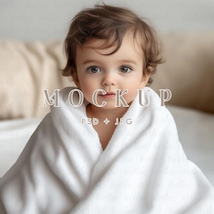 May include: A baby wrapped in a white hooded towel. The image has the word "MOCKUP" in a decorative font, with "PSD + JPG" below it. The baby has brown hair and is looking directly at the camera.