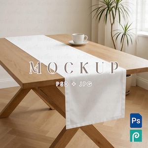 May include: A plain white rectangular table runner draped over a light brown wooden table. A white ceramic coffee cup sits on the runner. The image features the text MOCKUP PSD + JPG in the center and a small blue Ps icon in the corner.