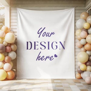K&ouml;nnte beinhalten: Ein wei&szlig;es Banner mit dem Text "Your DESIGN here" in Lila, flankiert von Ballonanordnungen in Creme-, Pfirsich- und Braunt&ouml;nen. Das Banner h&auml;ngt an einer Holzwand und bildet einen festlichen Hintergrund.