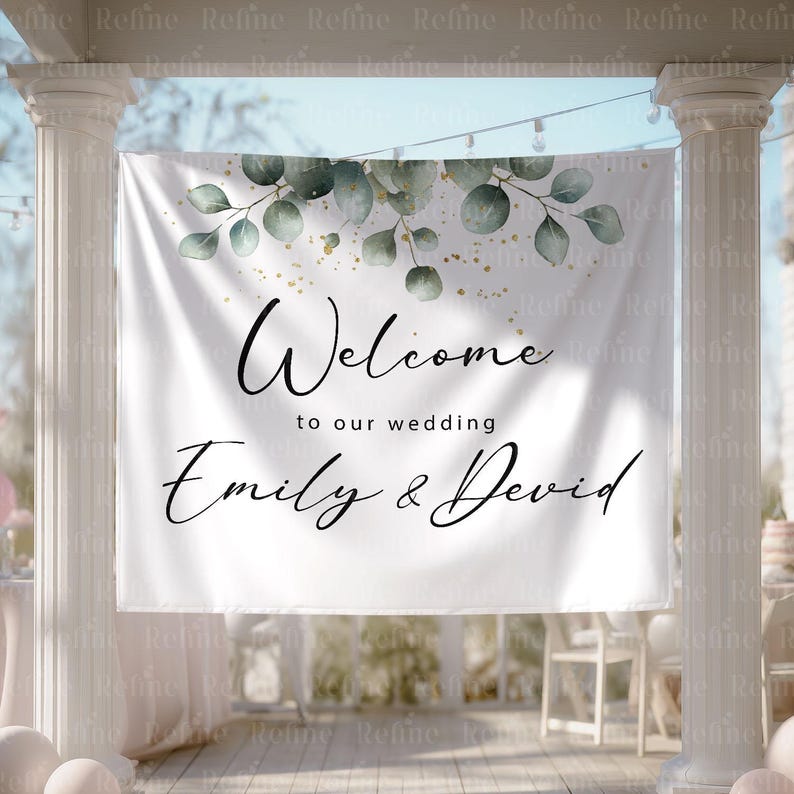 May include: A white banner with the text "Welcome to our wedding Emily & David" in elegant script. The banner is decorated with green eucalyptus leaves and gold accents, perfect for a wedding ceremony.
