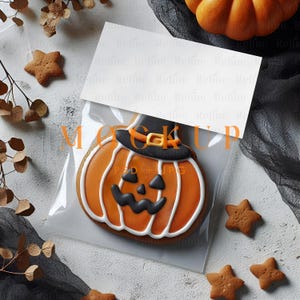 May include: A Halloween-themed image featuring a pumpkin-shaped cookie in a clear bag. The cookie is decorated with orange icing, a black hat, and a jack-o'-lantern face. Star-shaped cookies and a pumpkin are also visible.