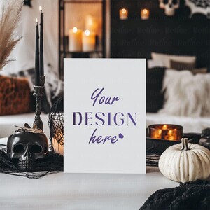 Op de afbeelding: Een Halloween-thema met een witte kaart met de tekst "Your DESIGN here" in paars. De sc&egrave;ne bevat een zwarte schedel, kaarsen, een witte pompoen en een kandelaar. De achtergrond is wazig.